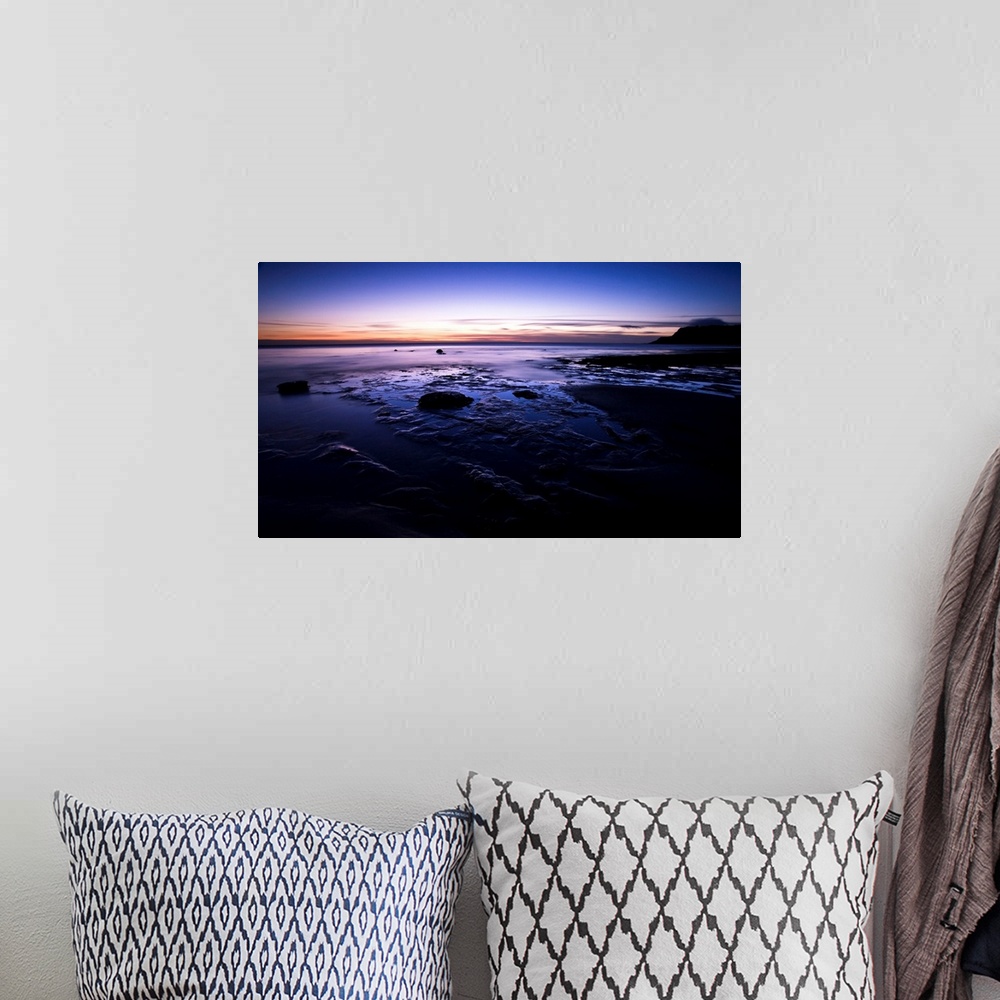A bohemian room featuring A dramatic seascape at dawn with deep purple magenta pink skies and clouds over wet sands.