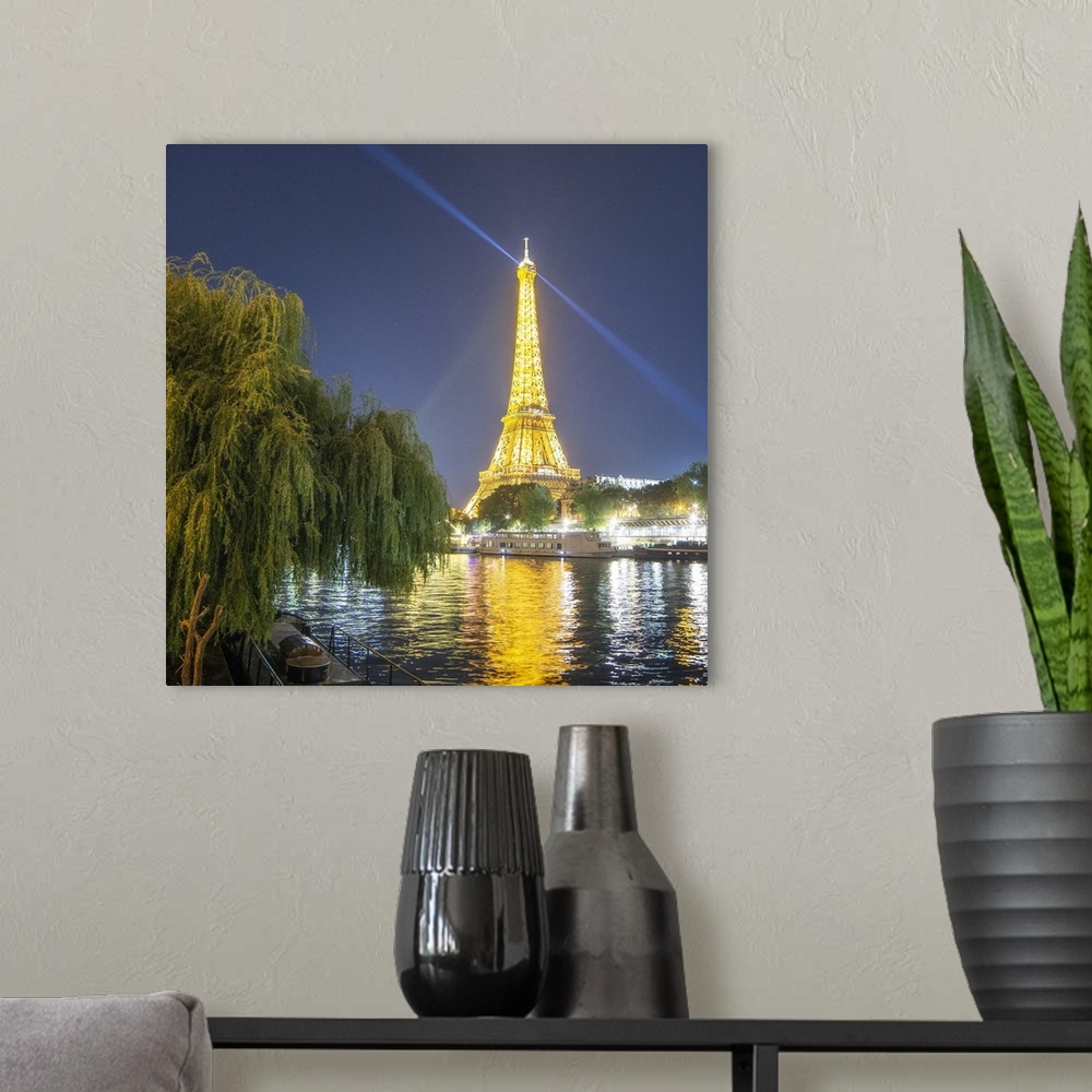 A modern room featuring National french monument Eiffel tower lighting at night with boat on the Seine river with trees o...