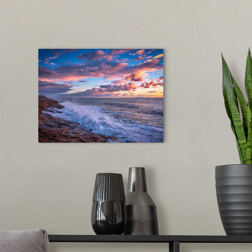 A modern room featuring Beautiful photograph of a warm, cloudy sunset over the ocean with crashing waves onto the rocky s...