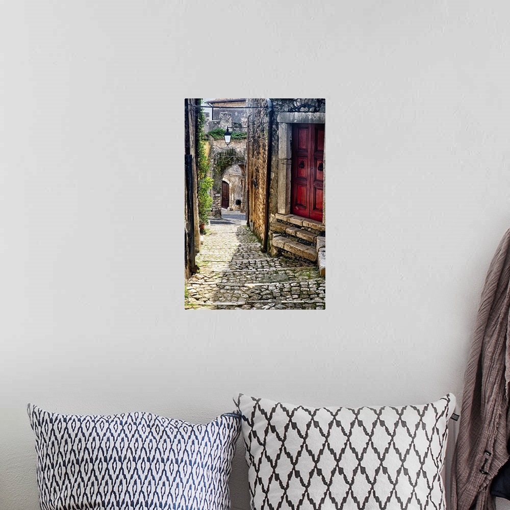 A bohemian room featuring Cobblestone street in Sermoneta, Italy, with a red door on the side.