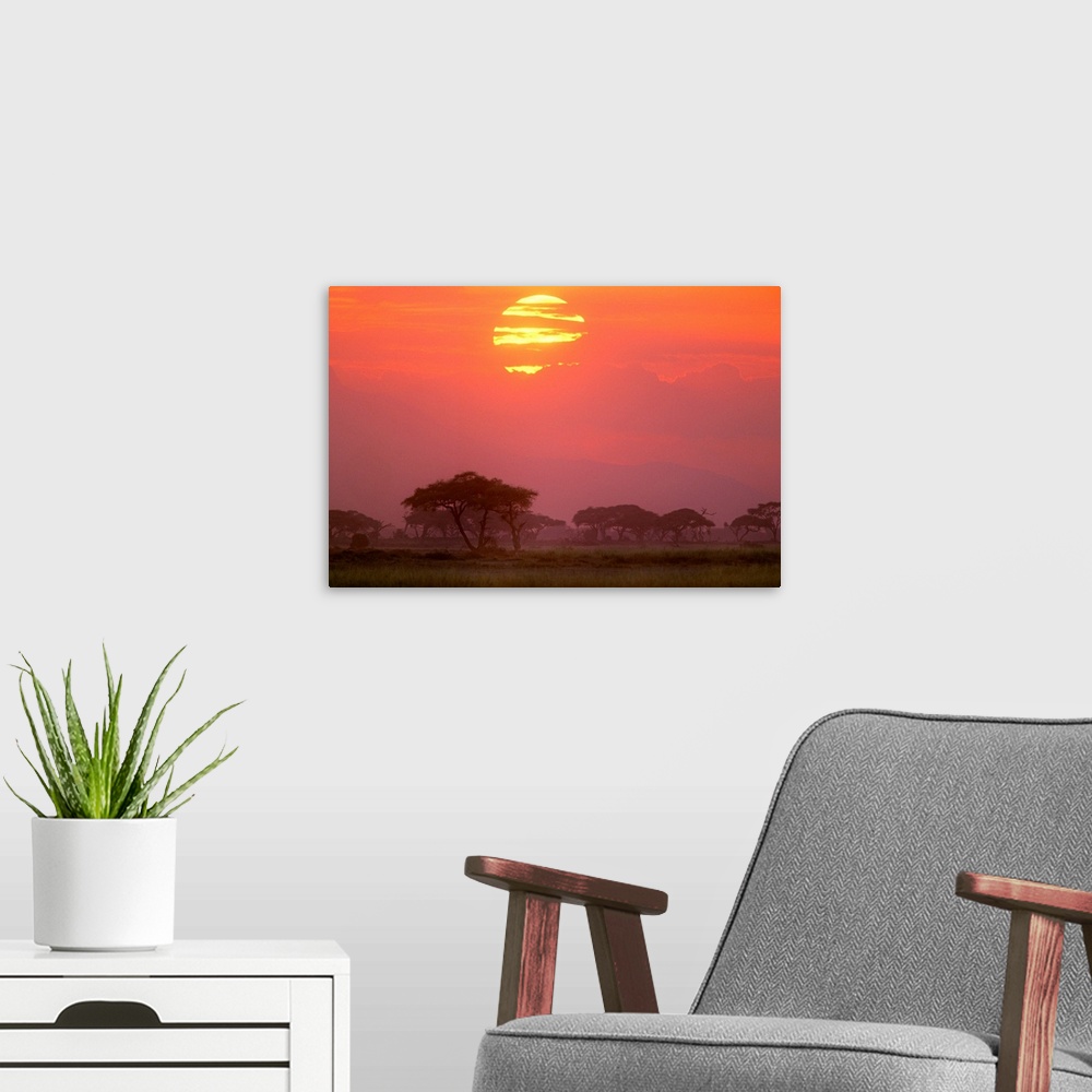 A modern room featuring Landscape photograph of the sun setting behind streaky clouds, over a Savanna landscape or grasse...