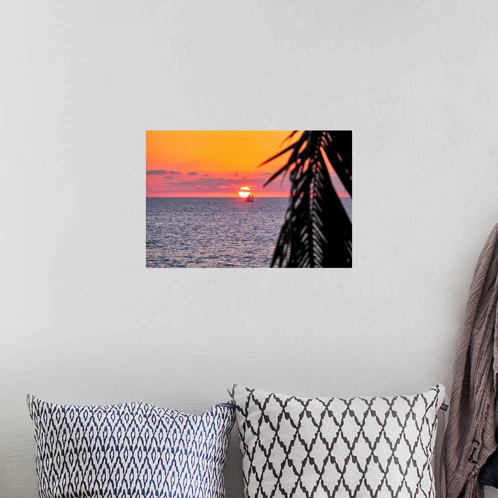 A bohemian room featuring A photo of sun setting behind a boat on water in Puerto Vallarta, Mexico with a palm tree leaf on...