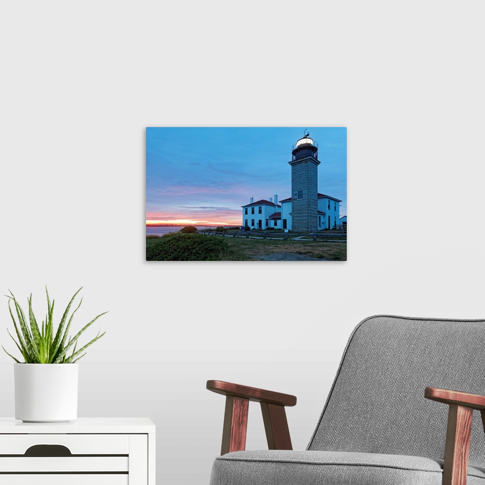 A modern room featuring Photograph of lighthouse and building near water's edge under a cloudy sky at dusk.