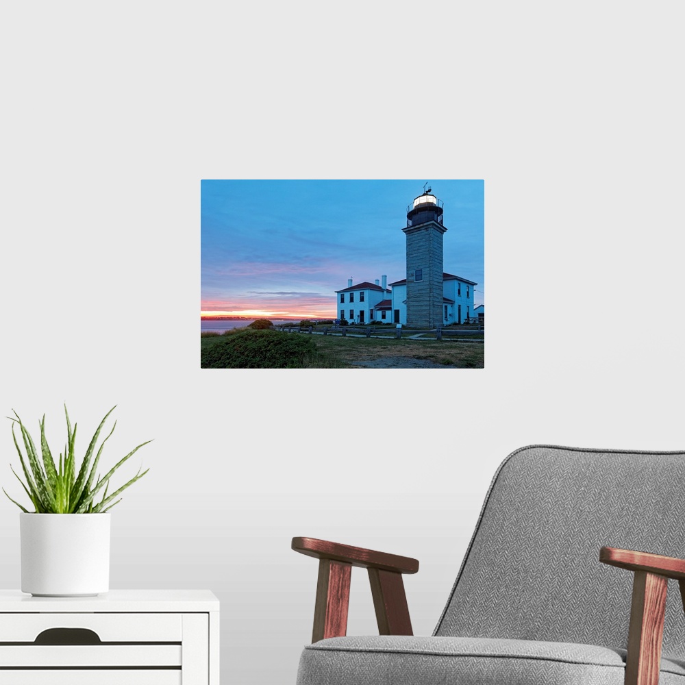 A modern room featuring Photograph of lighthouse and building near water's edge under a cloudy sky at dusk.