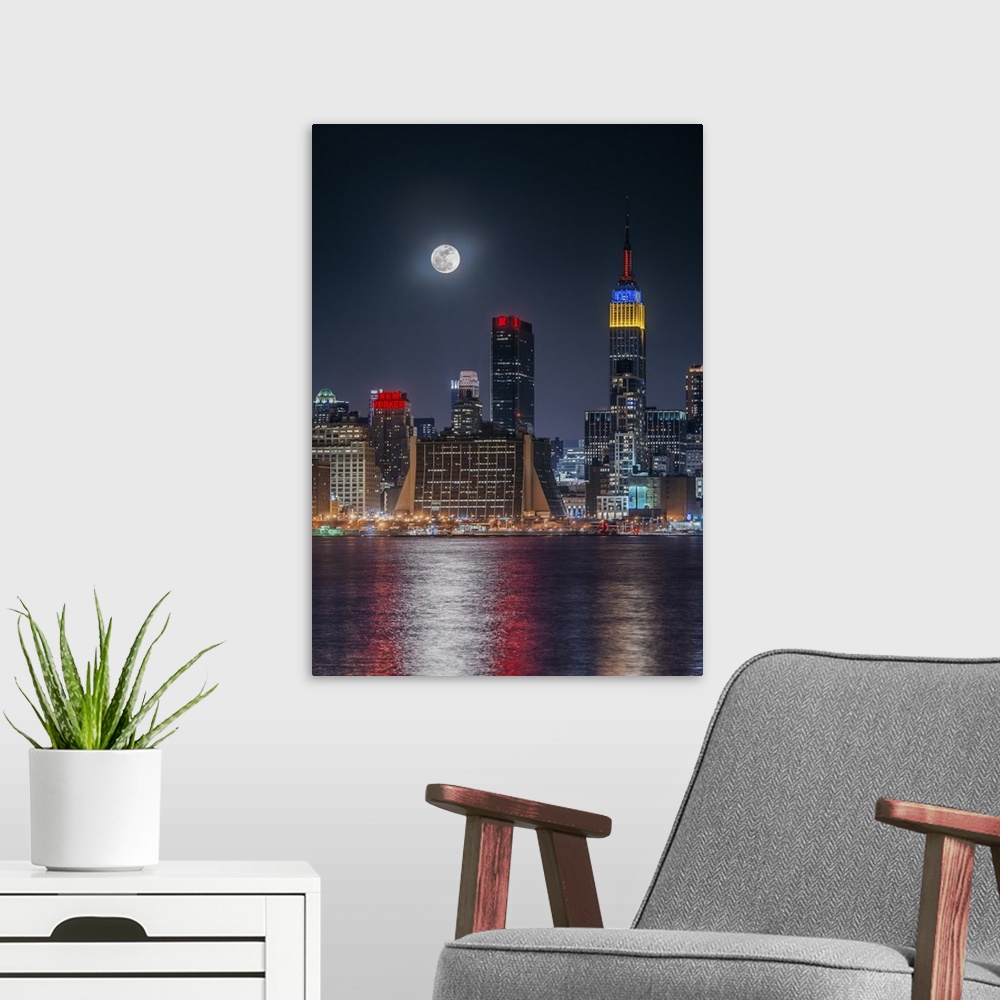 A modern room featuring Large full moon shining over the Manhattan skyline, reflected in the bay below.