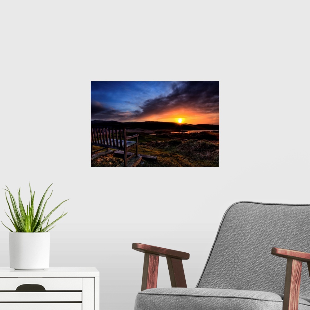 A modern room featuring A wooden seat looking out over a Scottish view to a Loch with a golden sunset and dramatic sky.