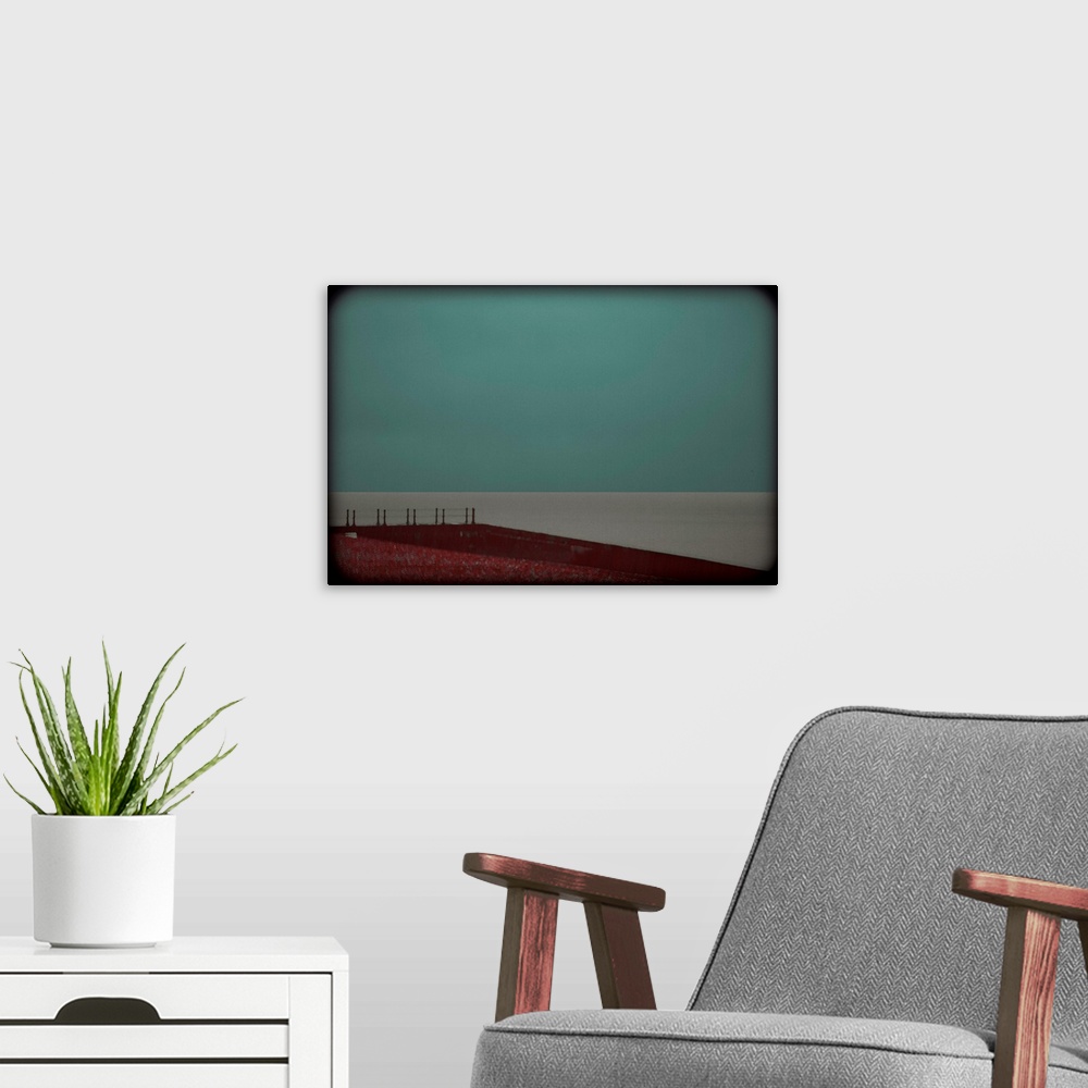 A modern room featuring Minimalist photograph of a red landing leading up to a calm, gray sea with a turquoise sky and da...