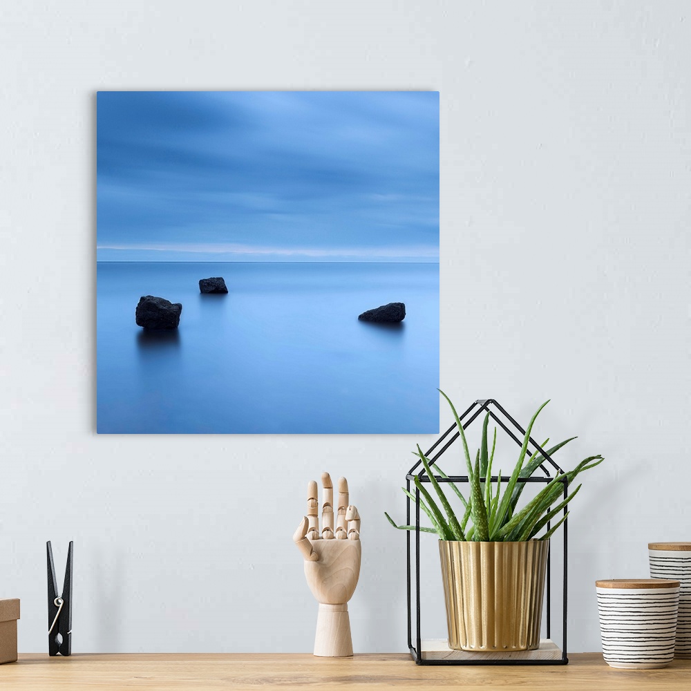 A bohemian room featuring A zen calm minimal minimalist cool deep blue image of three rocks in a flat calm sea.