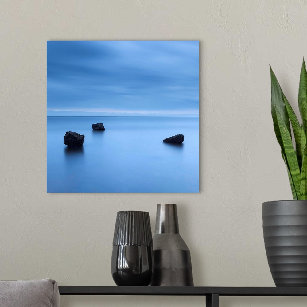 A modern room featuring A zen calm minimal minimalist cool deep blue image of three rocks in a flat calm sea.