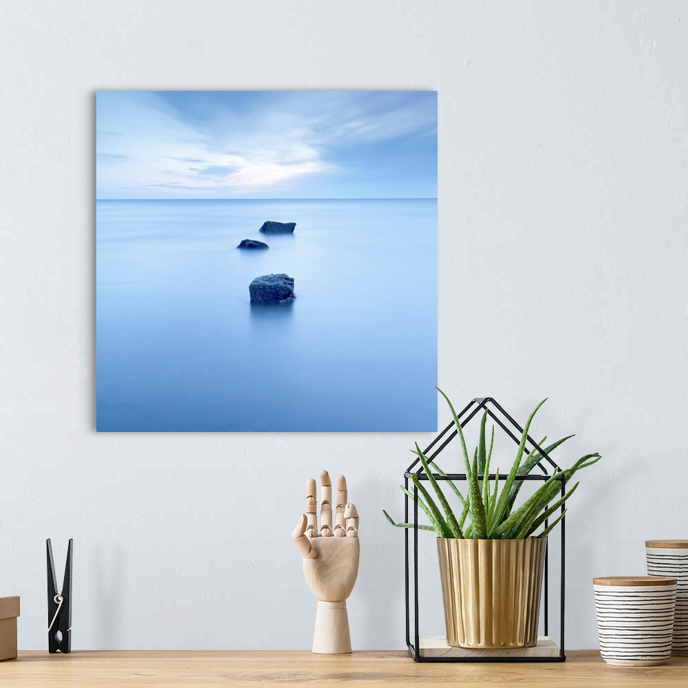A bohemian room featuring Large, square photograph of three rocks rising up from calm waters, beneath a partly cloudy sky.