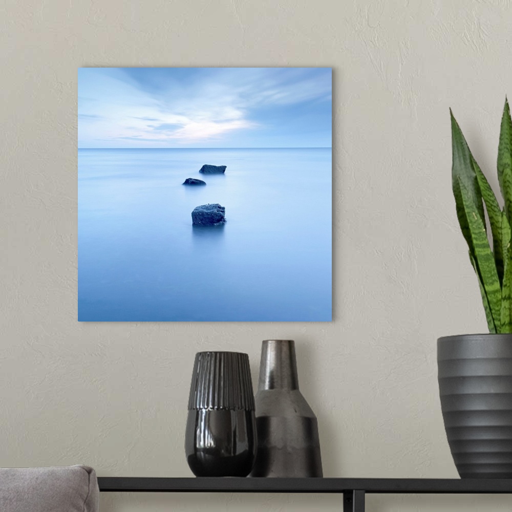 A modern room featuring Large, square photograph of three rocks rising up from calm waters, beneath a partly cloudy sky.
