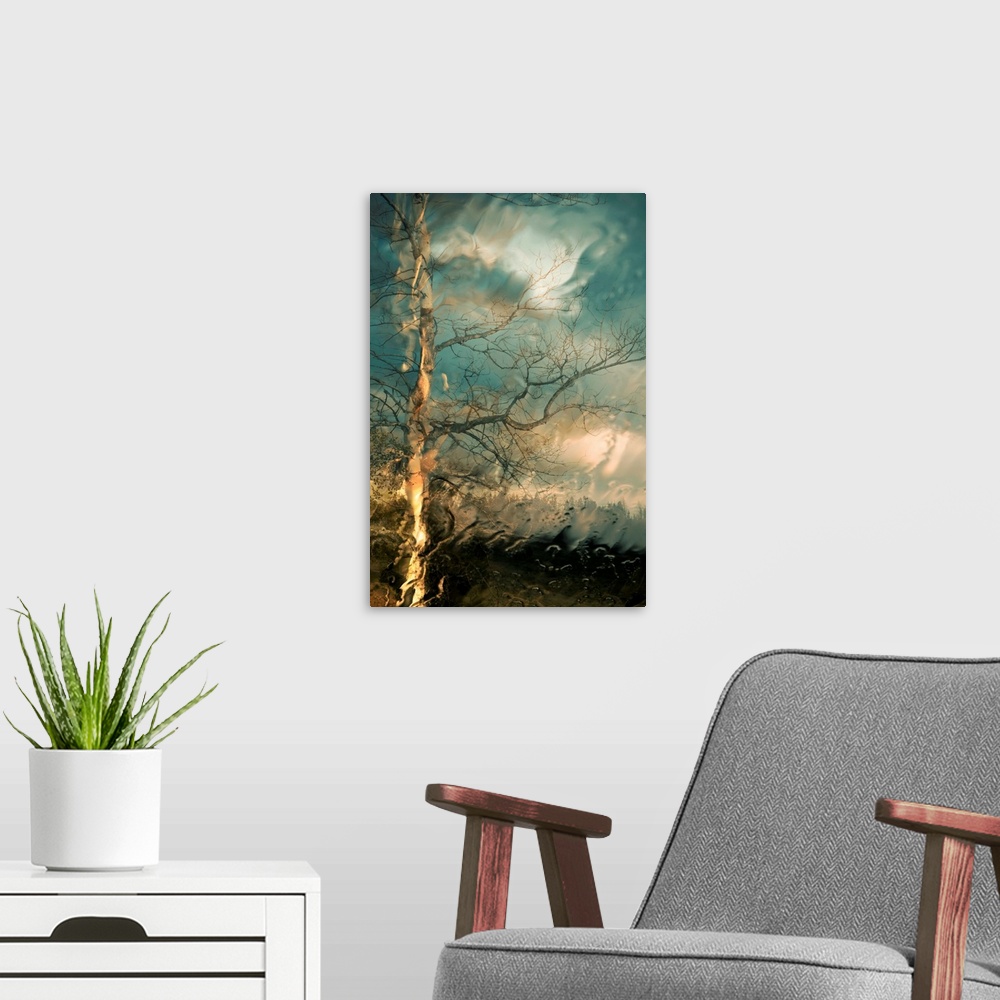 A modern room featuring Vertical, large wall picture of a big tree with bare branches on a hill below a sky of swirling, ...