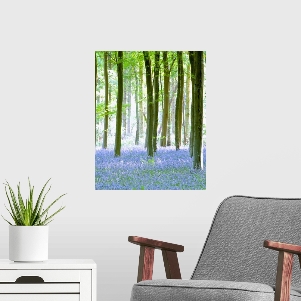 A modern room featuring Vertical painting on canvas of a forest with wildflowers sprinkled on the ground beneath them.