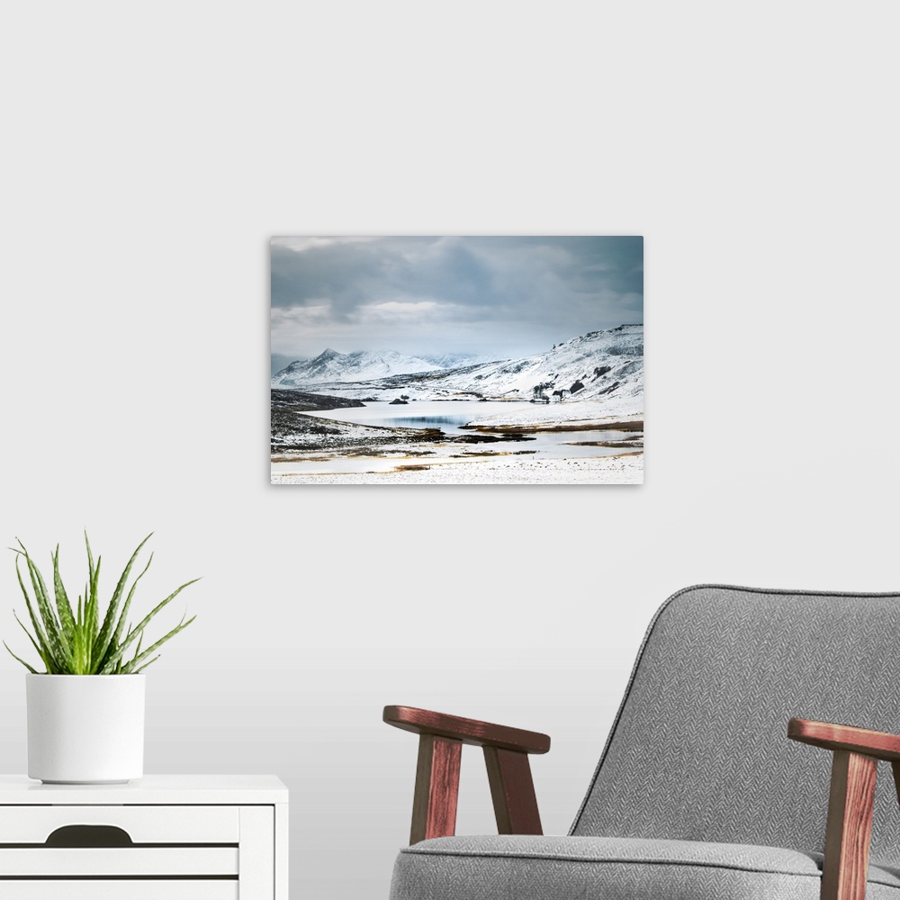 A modern room featuring Scottish Mountains in the snow with a small cottage beside a lake.