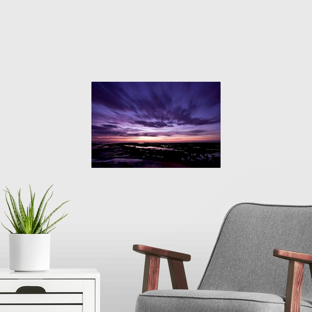 A modern room featuring A dramatic seascape at dawn with deep purple magenta pink skies and clouds over wet sands.