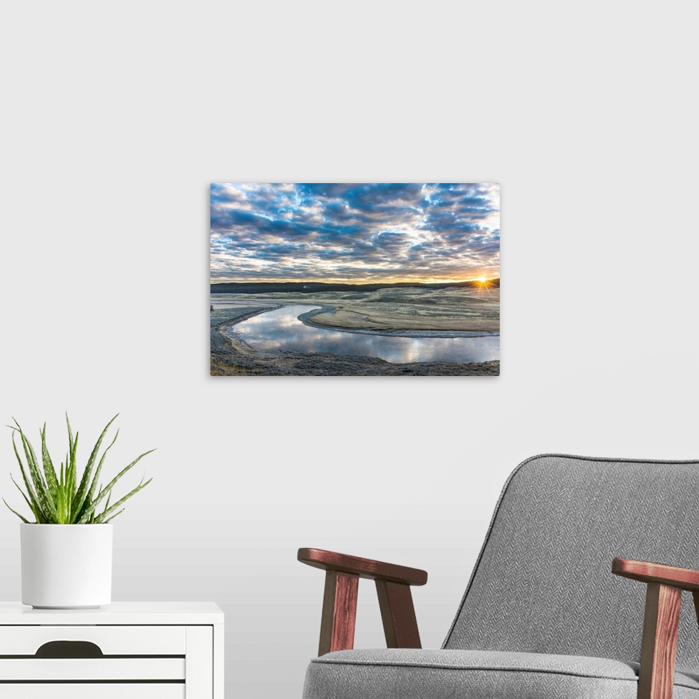 A modern room featuring Fine art photograph of the sun on the horizon by the Yellowstone River with cloudy skies above.