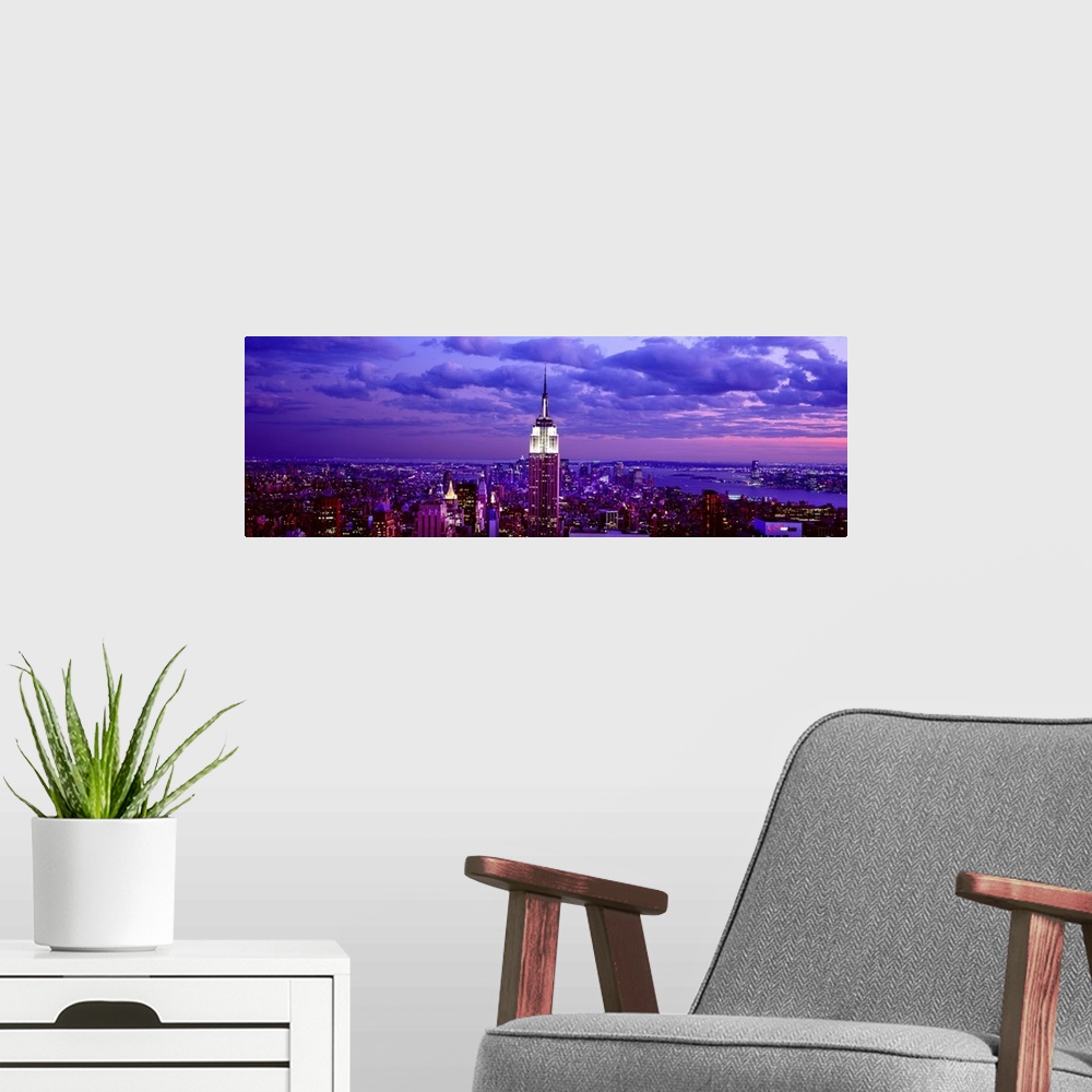 A modern room featuring This is a large aerial photograph taken of NYC at dusk with all of the buildings lit and the empi...