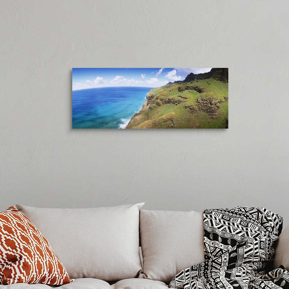 A bohemian room featuring Panoramic photograph of rocky grass covered cliff near water's edge under a cloudy sky.