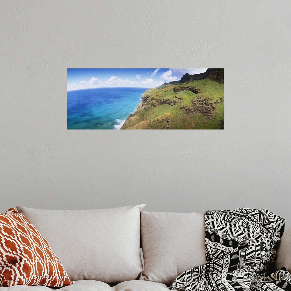 A bohemian room featuring Panoramic photograph of rocky grass covered cliff near water's edge under a cloudy sky.