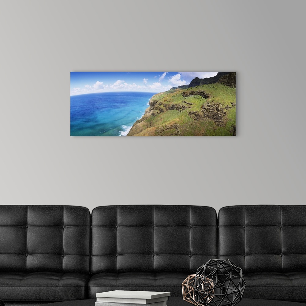 A modern room featuring Panoramic photograph of rocky grass covered cliff near water's edge under a cloudy sky.