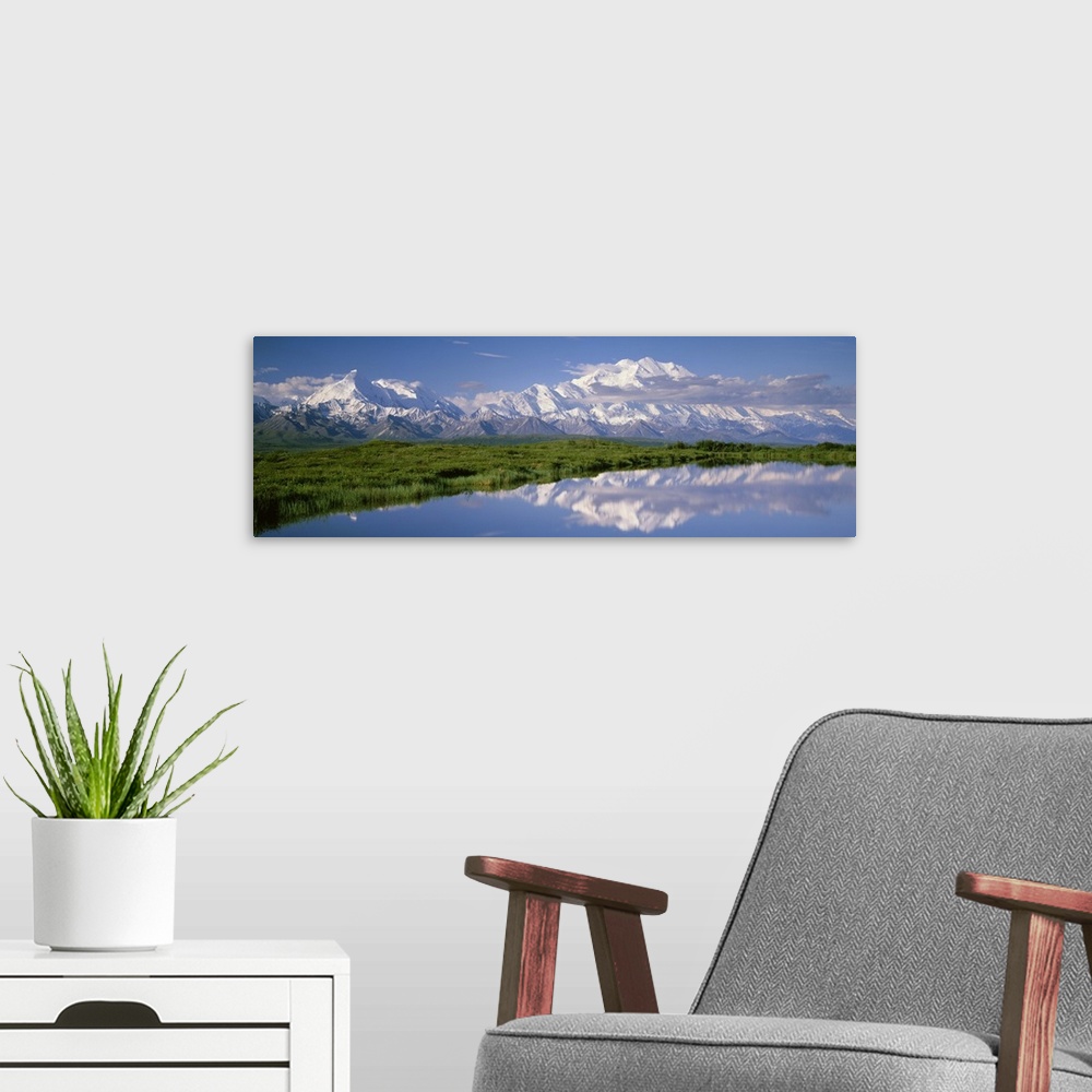 A modern room featuring A snow covered mountain range is photographed in panoramic view with a large field shown just in ...