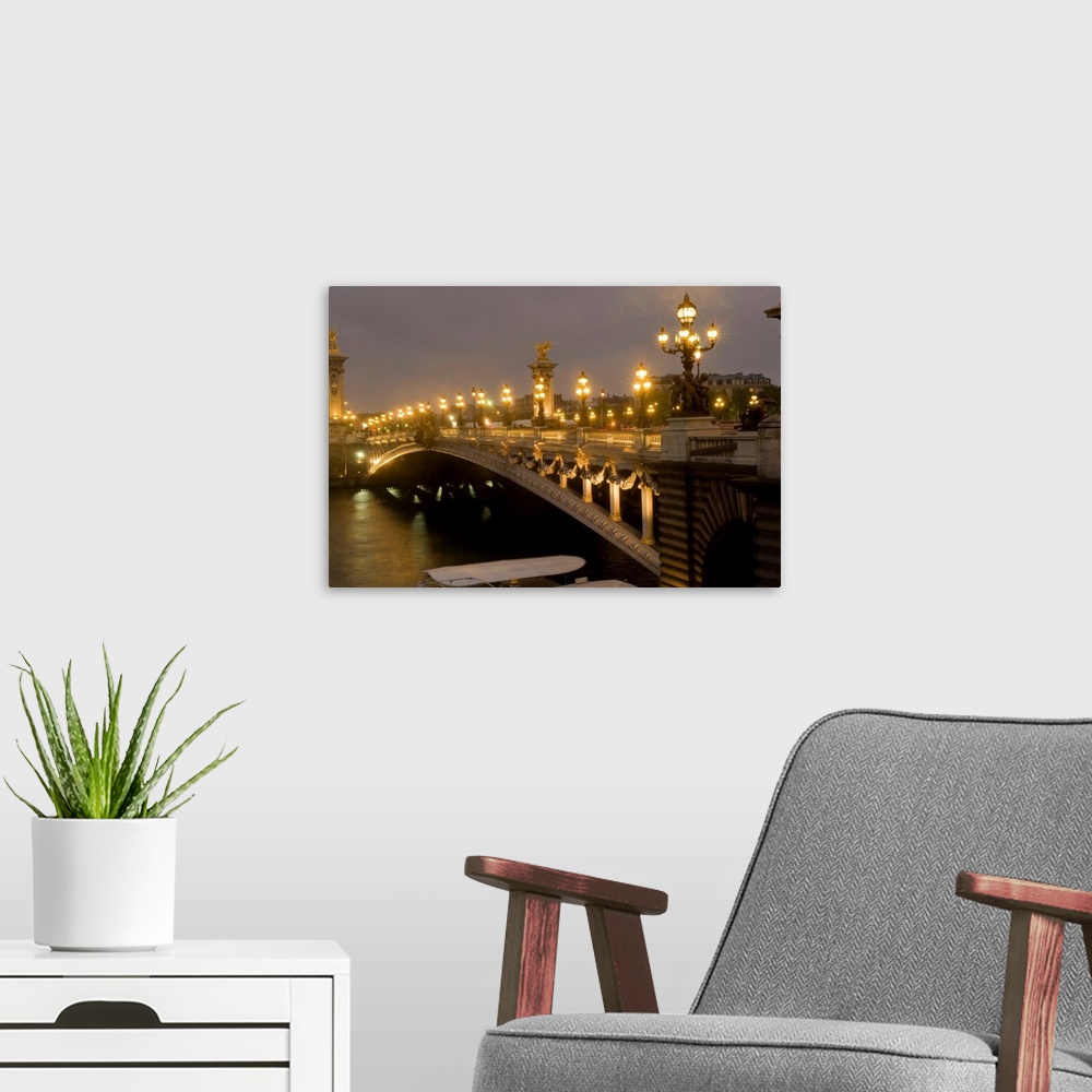 A modern room featuring Big photo on canvas of a bridge lit up going over a river in France.