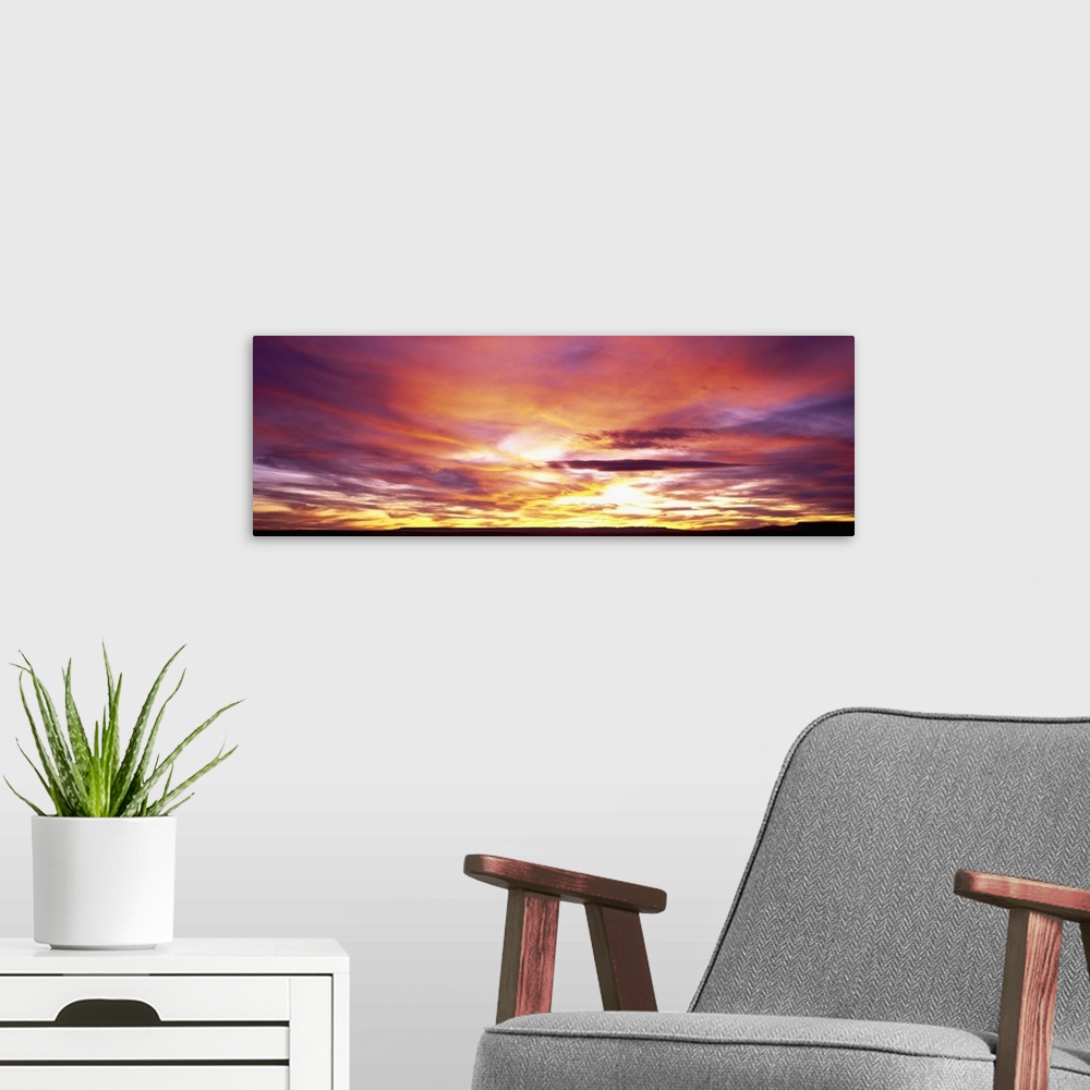 A modern room featuring A panoramic photograph of clouds lit up in brilliant colors from the sun below the horizon.