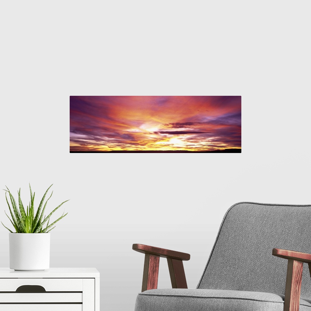 A modern room featuring A panoramic photograph of clouds lit up in brilliant colors from the sun below the horizon.