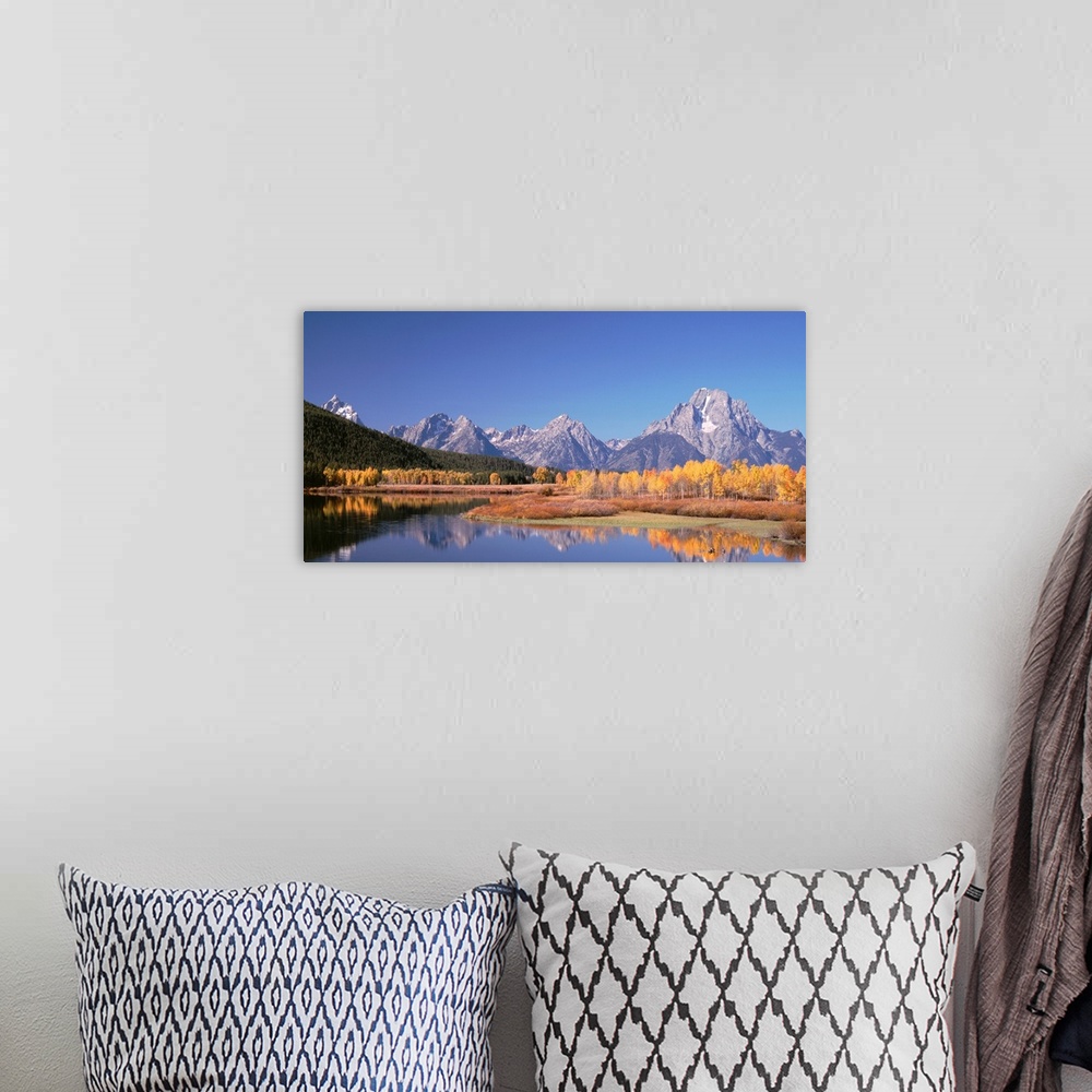 A bohemian room featuring Trees and tall mountain peaks reflect in the calm surface of a lake in this landscape photograph.