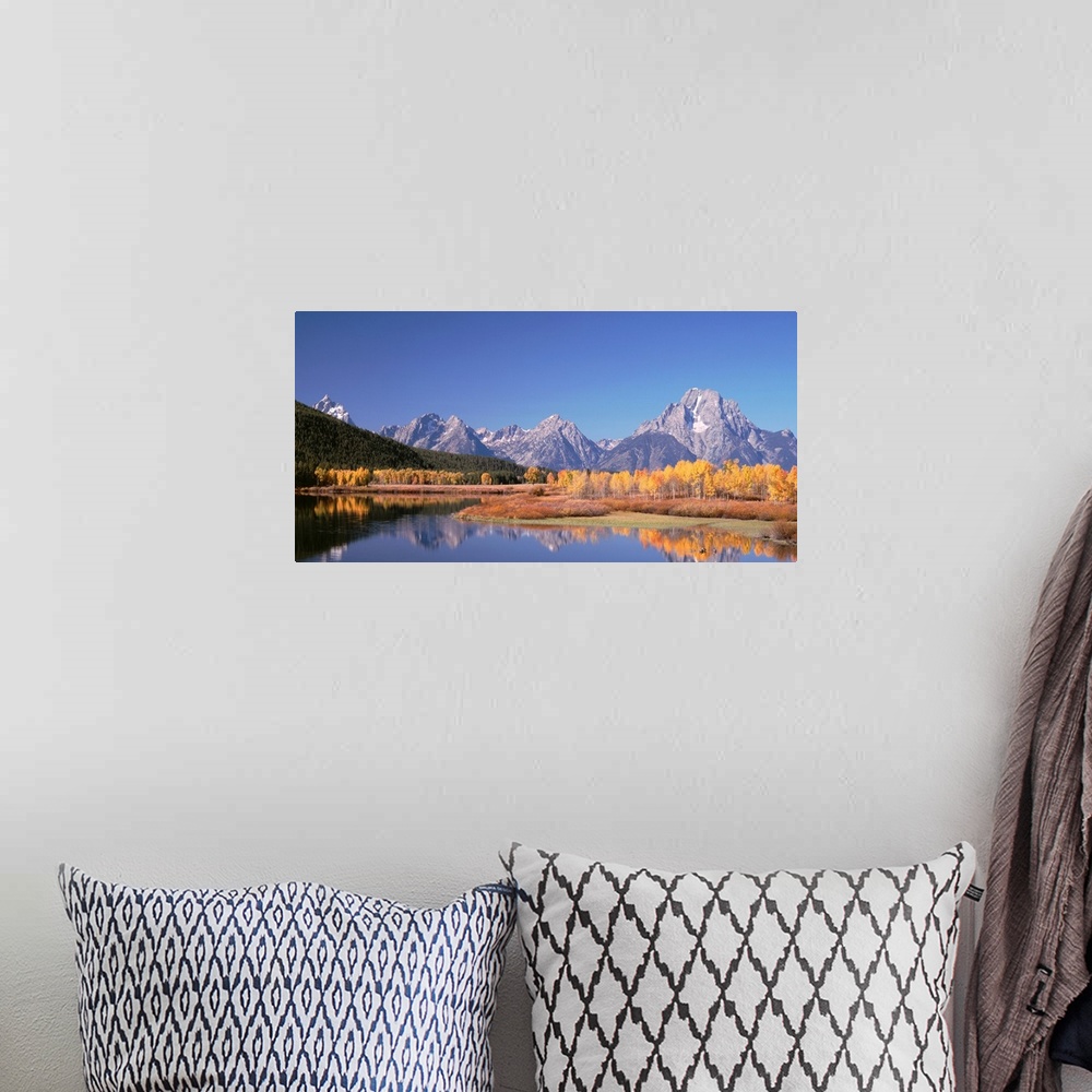 A bohemian room featuring Trees and tall mountain peaks reflect in the calm surface of a lake in this landscape photograph.