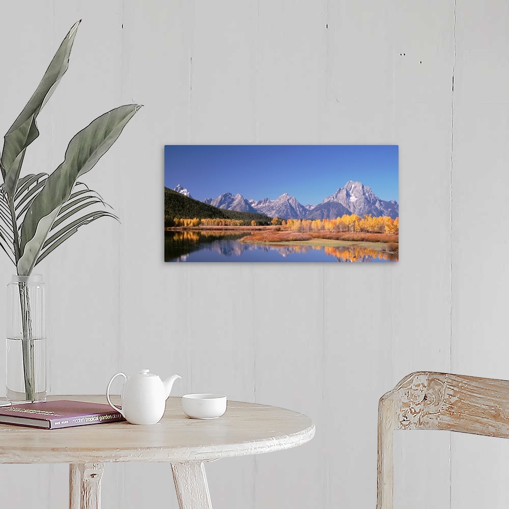 A farmhouse room featuring Trees and tall mountain peaks reflect in the calm surface of a lake in this landscape photograph.