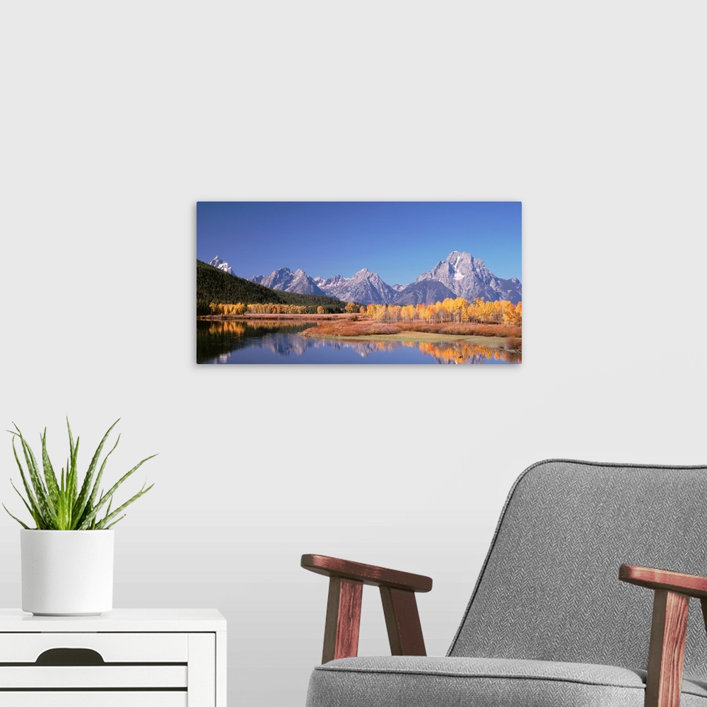 A modern room featuring Trees and tall mountain peaks reflect in the calm surface of a lake in this landscape photograph.
