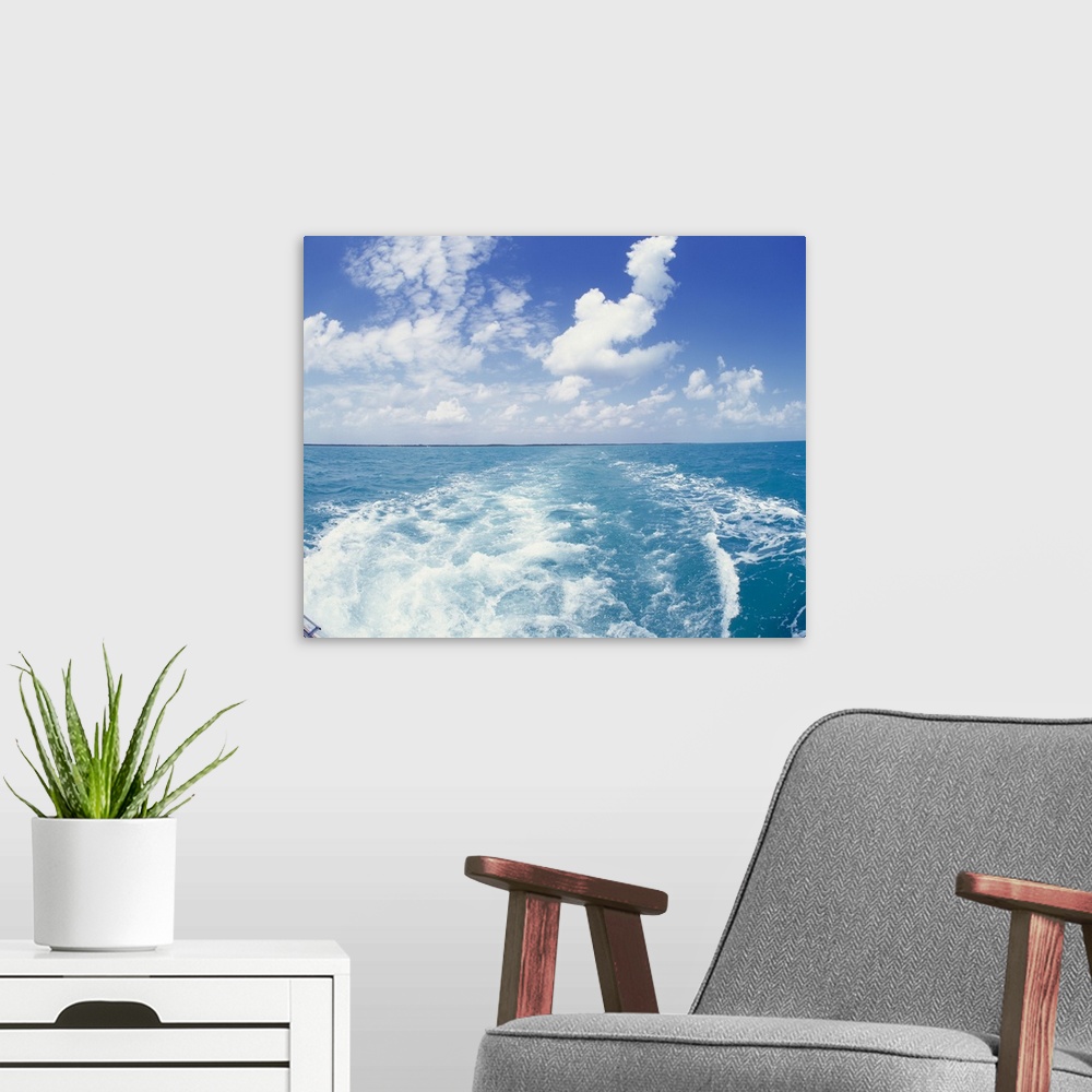 A modern room featuring Photo on canvas of the ocean with land in the far distance and puffy clouds above looking from be...