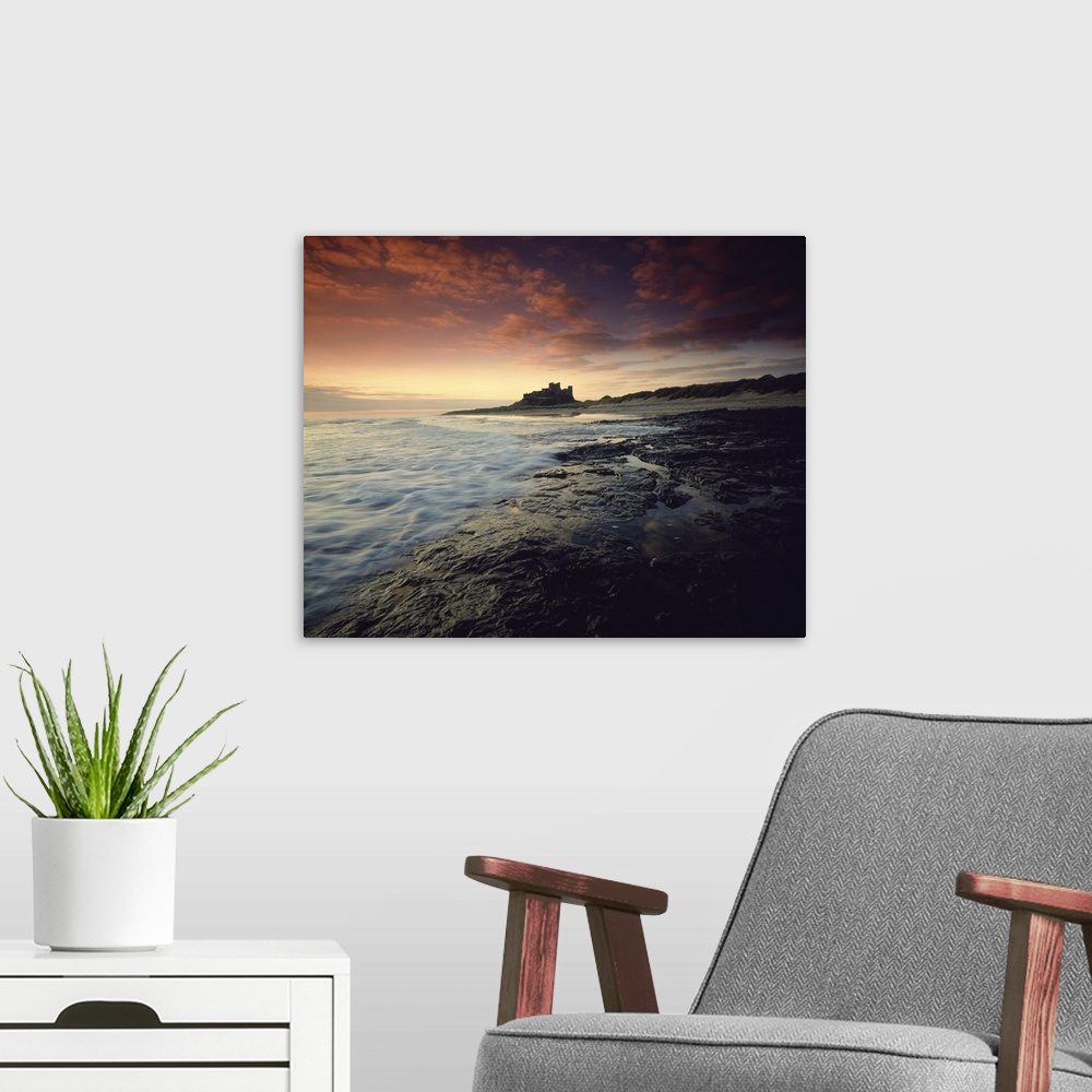 A modern room featuring Oversized landscape photograph of a rocky shoreline in England at sunset, Bam burgh Castle can be...