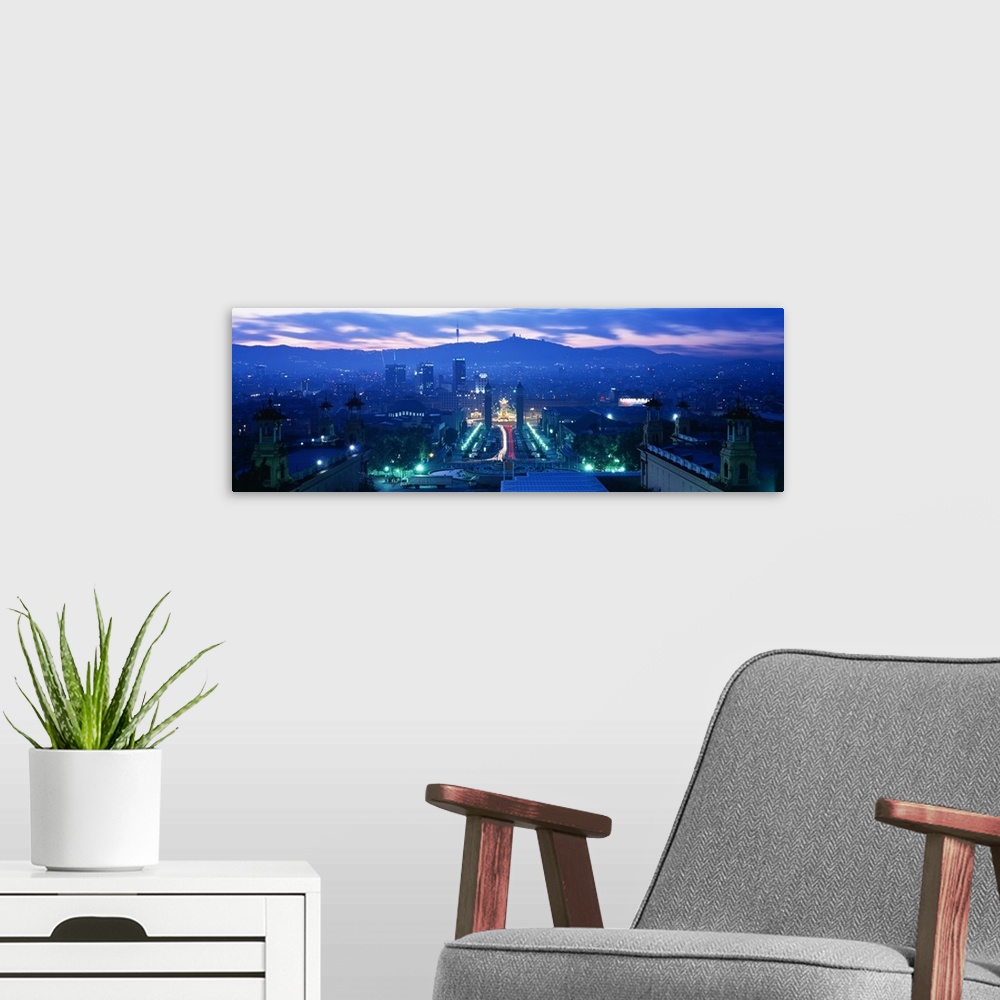 A modern room featuring Giant, high angle photograph of Barcelona, lit at night, mountains in the background beneath a mo...
