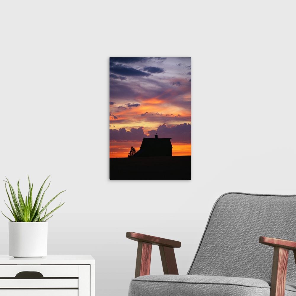 A modern room featuring Vertical panoramic photograph of farm house silhouette at dusk under a cloudy and colorful sky.