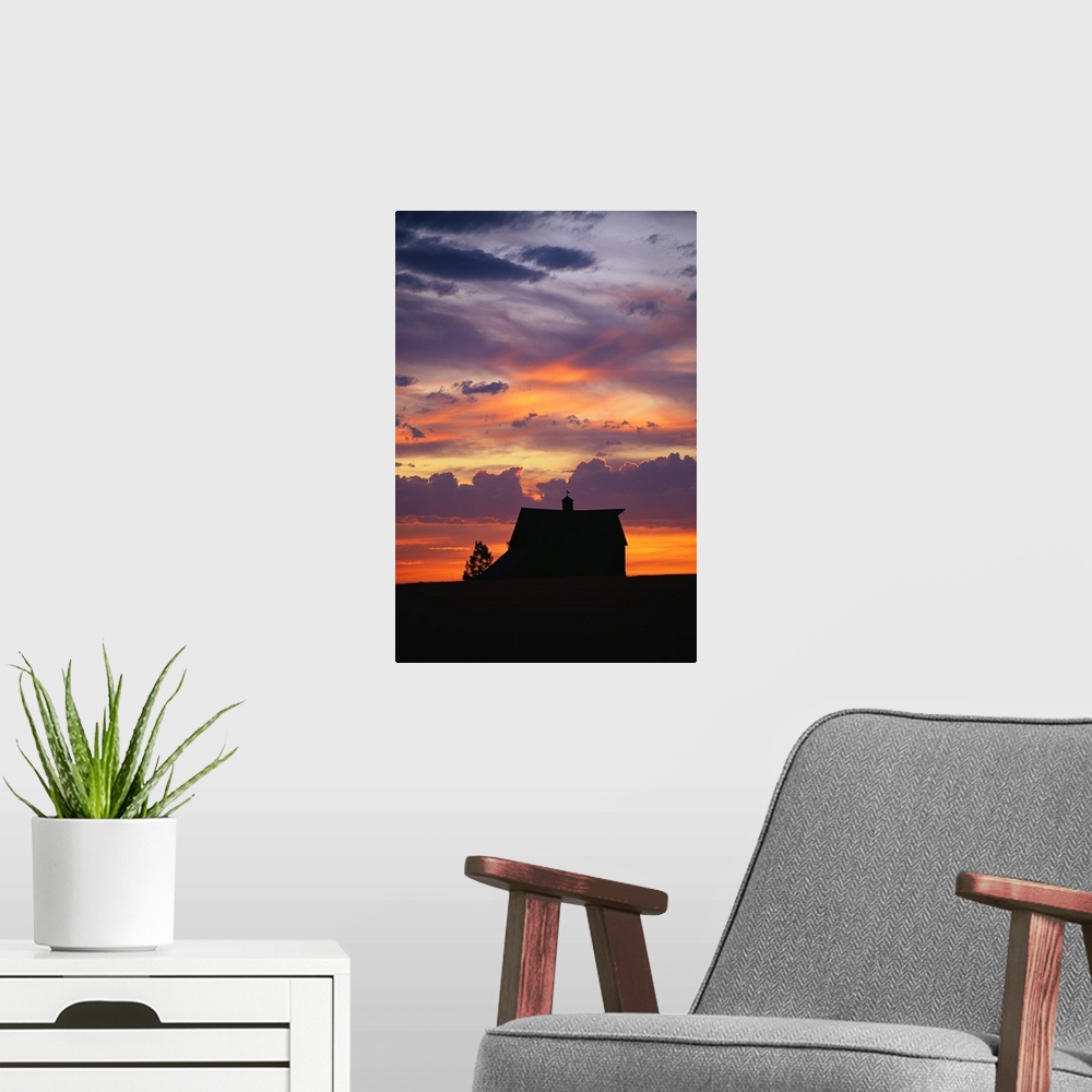 A modern room featuring Vertical panoramic photograph of farm house silhouette at dusk under a cloudy and colorful sky.