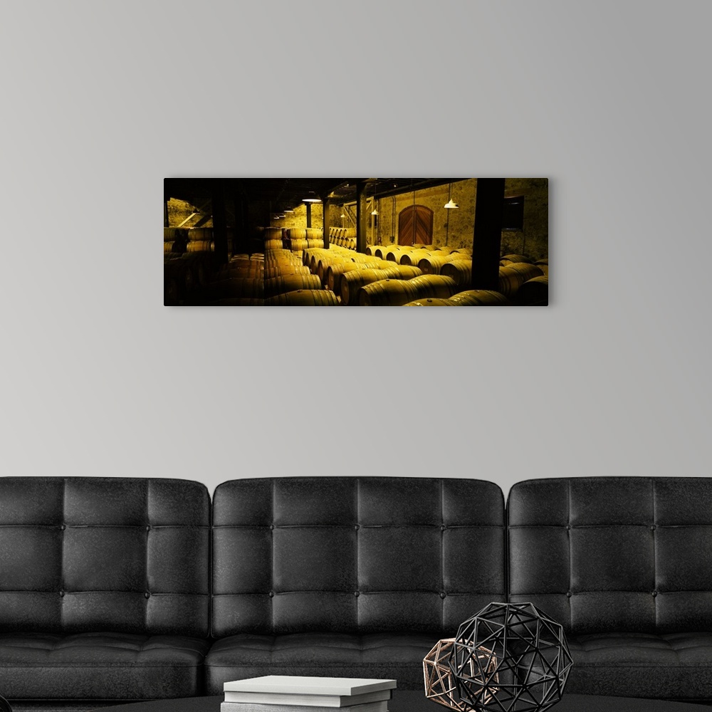 A modern room featuring Large, landscape photograph of a partially lit cellar with stone walls, full of wine barrels, in ...