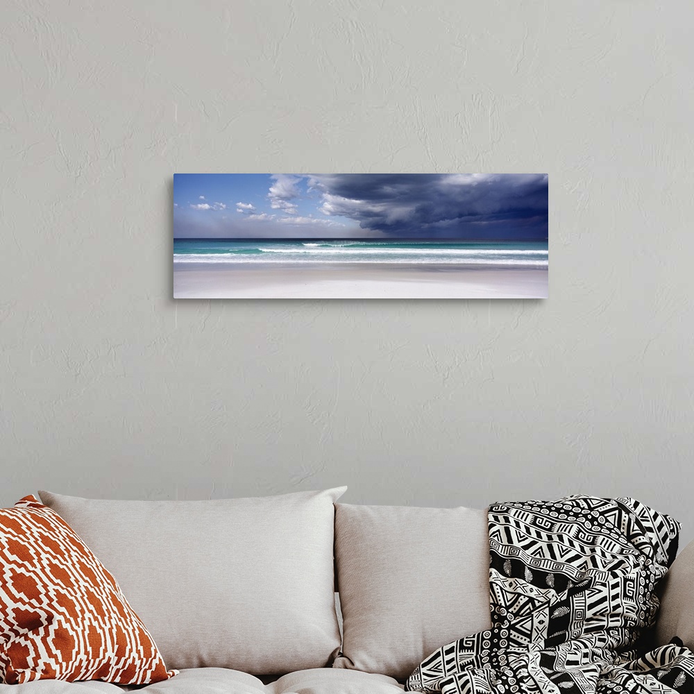 A bohemian room featuring Panoramic photo print of an ocean with crashing waves and blue skies on the left and storm clouds...