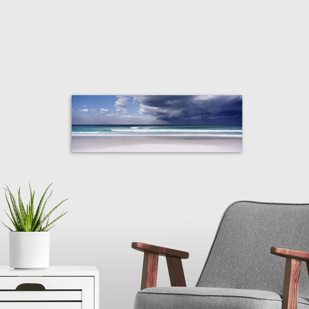 A modern room featuring Panoramic photo print of an ocean with crashing waves and blue skies on the left and storm clouds...