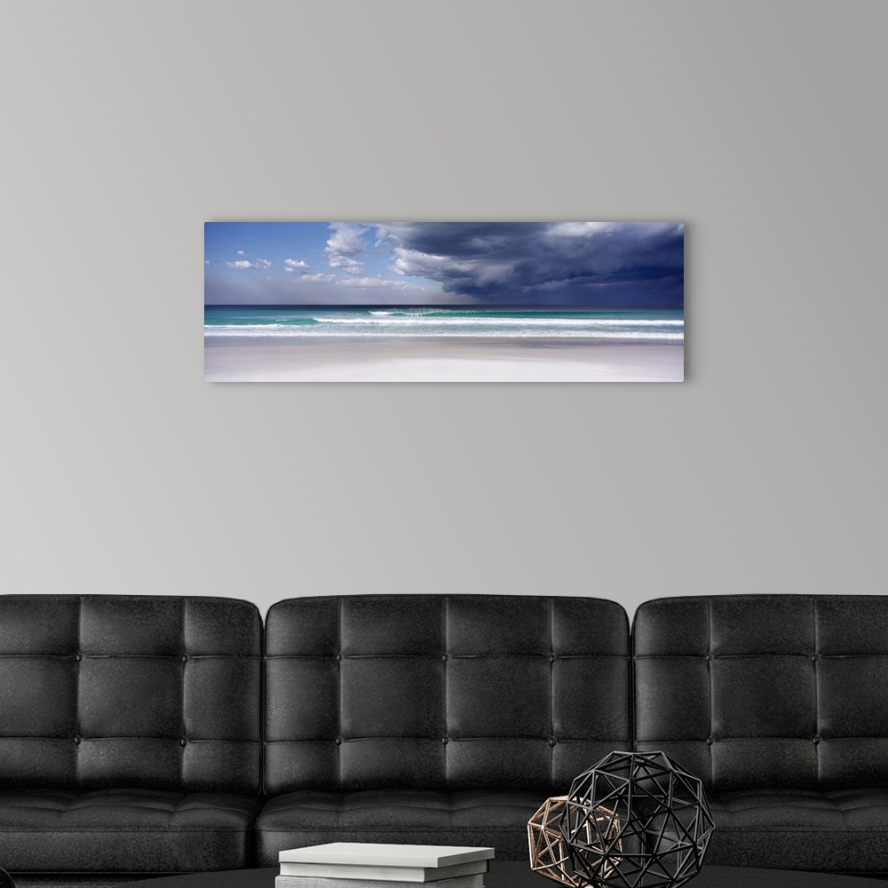 A modern room featuring Panoramic photo print of an ocean with crashing waves and blue skies on the left and storm clouds...