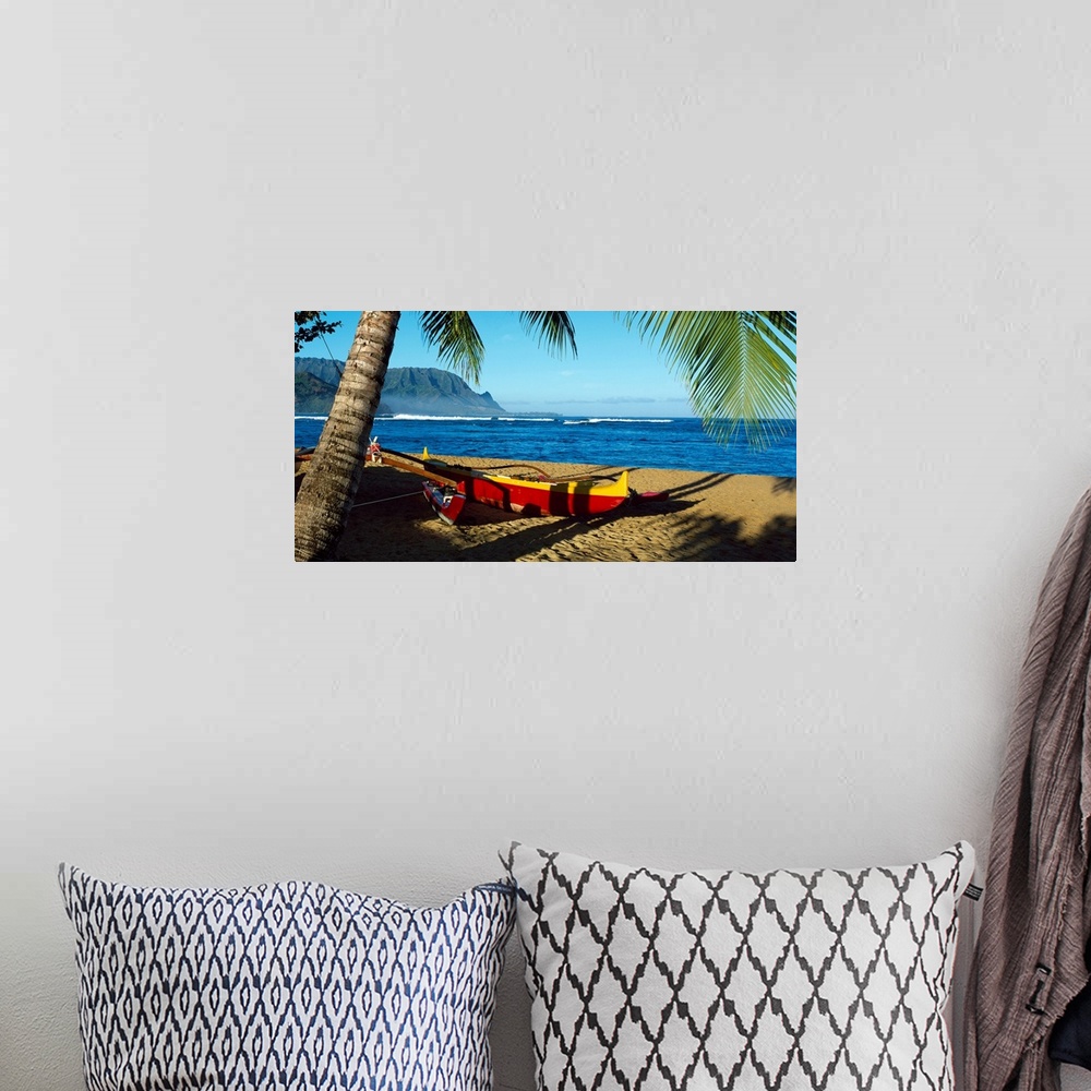 A bohemian room featuring Oversize wall art of a landscape photograph of a sailboat pulled up the shore and resting in the ...