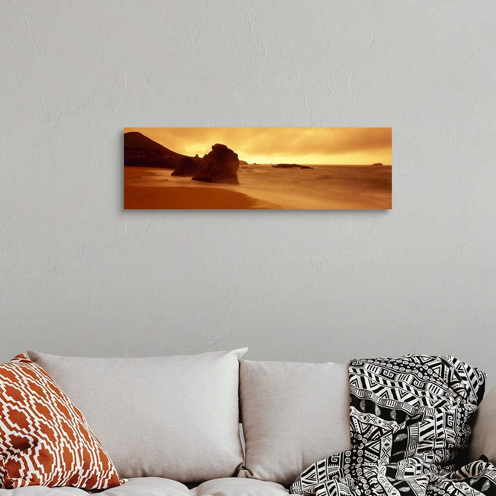 A bohemian room featuring Panoramic photograph of shoreline with huge rock formation in sand and large mountain in the dist...