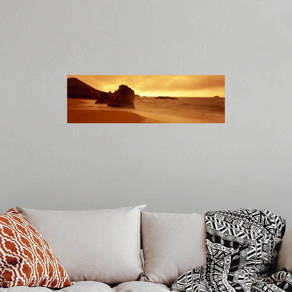 A bohemian room featuring Panoramic photograph of shoreline with huge rock formation in sand and large mountain in the dist...