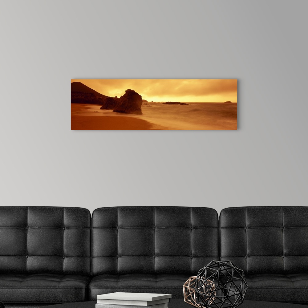 A modern room featuring Panoramic photograph of shoreline with huge rock formation in sand and large mountain in the dist...
