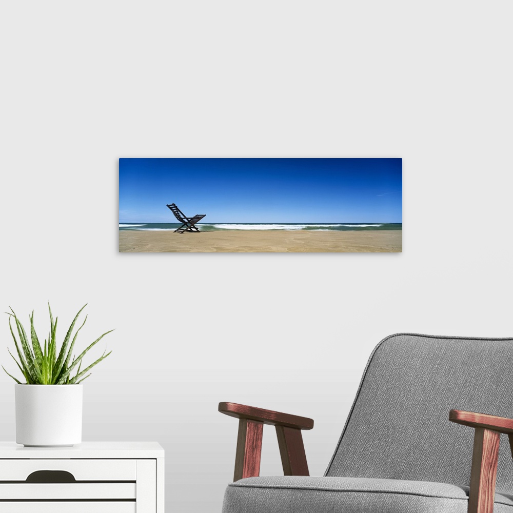 A modern room featuring Huge panoramic piece of a lone beach chair skewed to the left sitting in the sand with waves cras...