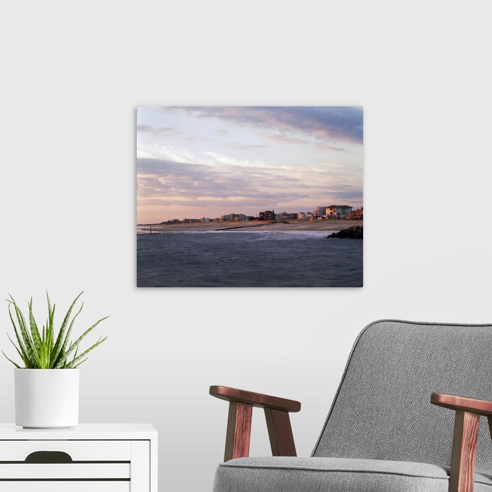 A modern room featuring This large piece is a photograph taken on the water looking at the beach coast that is lined with...