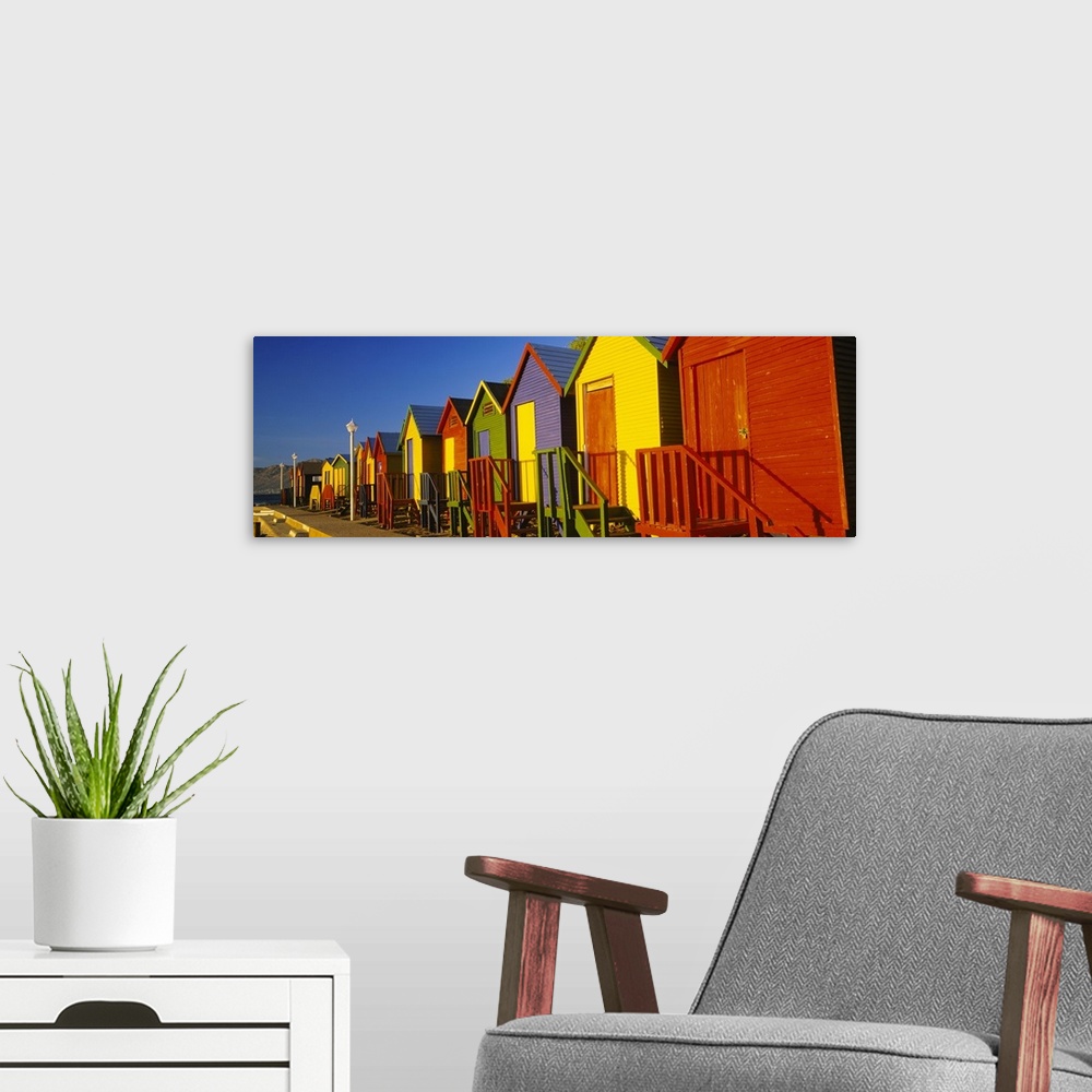 A modern room featuring Panoramic photograph displays a line of vibrantly colored seaside shacks on a sunny day.  In the ...