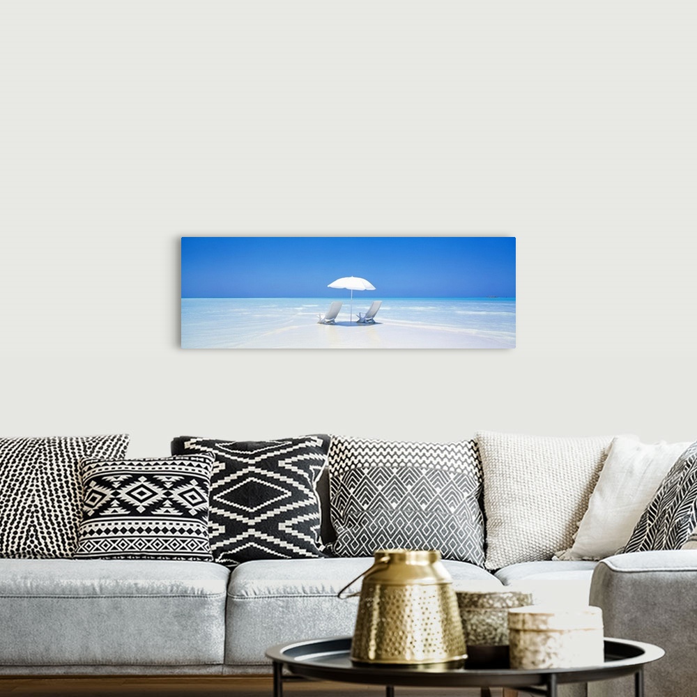 A bohemian room featuring A panoramic photograph displaying two chairs sitting underneath an umbrella on a sandy beach in M...