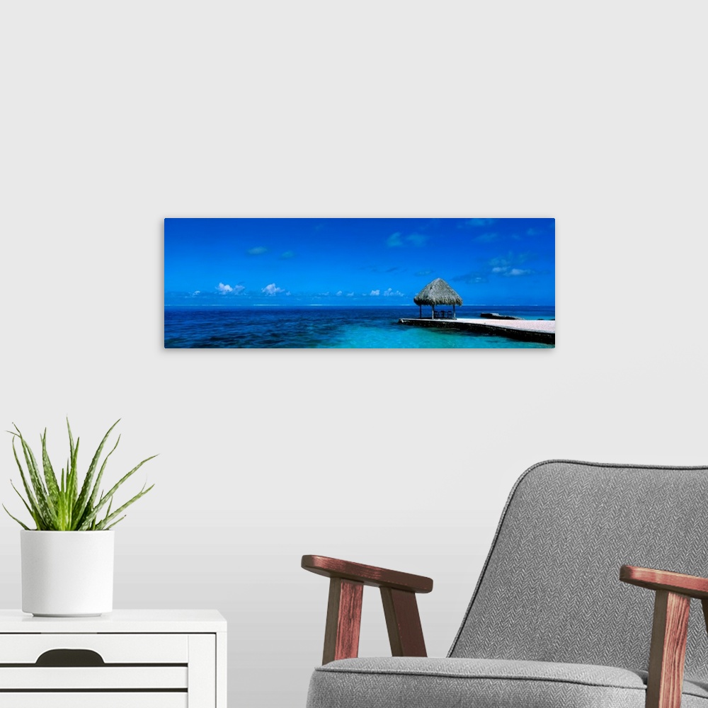 A modern room featuring This large wall art is a sweeping panoramic photograph of the ocean horizon and a single shady sh...